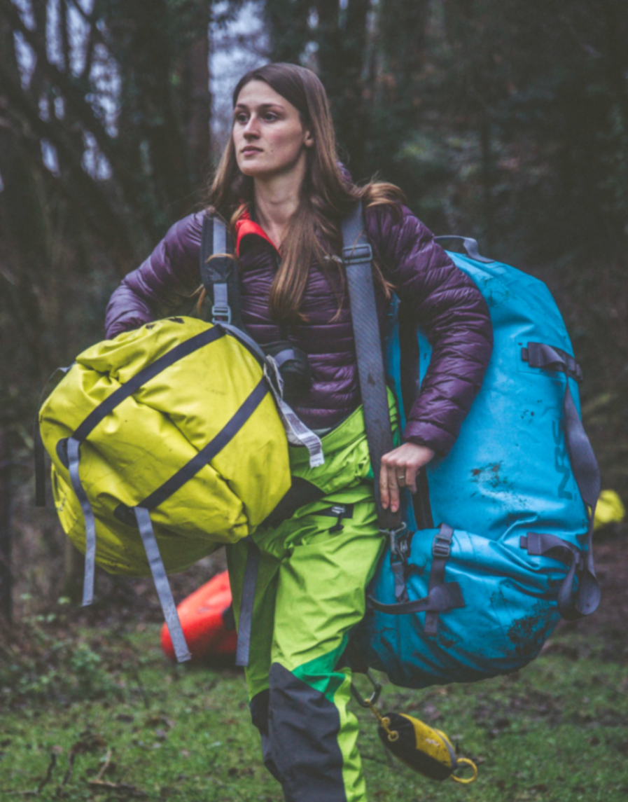 Laura carrying brightly coloured expedition dry bags through a forest